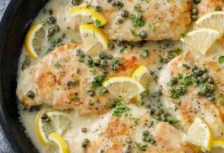 a skillet of chicken piccata garnished with lemon slices