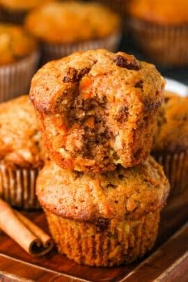 two Carrot Muffins stacked with one muffin with a bite taken out and a cinammon stick