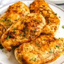 4 air fryer chicken breasts on a plate with green beans in the background